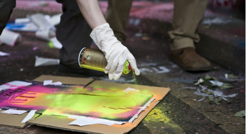 Gloved hand applying spray paint over a stencil.